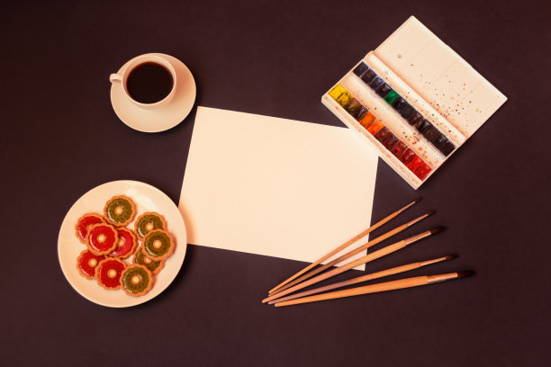 一杯咖啡，甜饼干草莓果冻和猕猴桃果冻，水彩画颜料，画笔和纸在黑暗的背景。图片下载