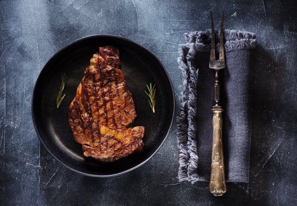 煎肋眼牛排在一个盘子和老肉叉，俯视图图片下载