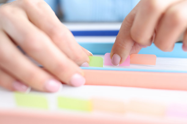 女性的手正在众多贴着彩色贴纸的纸张中寻找文件图片下载