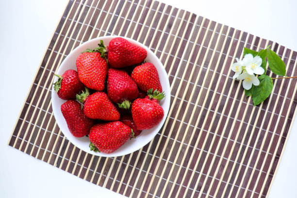 白色盘子上放着成熟的新鲜草莓和茉莉花图片下载