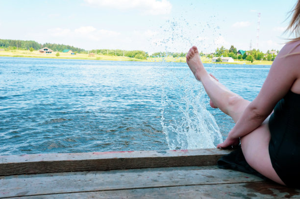 穿着泳衣的女孩坐在码头上，在水面上踢脚图片下载