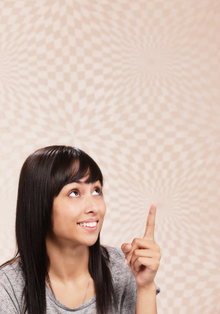 美丽的年轻女子看起来高兴和有点惊讶，因为她指向上方的图案背景图片下载