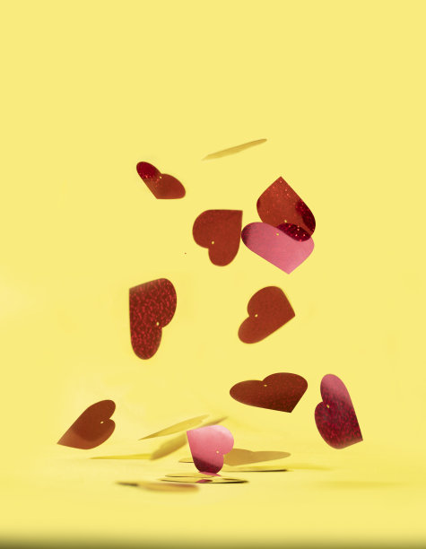 垂直拍摄的坠落红色心形的闪光纸屑孤立在黄色的背景图片下载