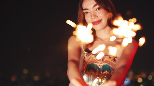 一个兴高采烈的年轻女子在户外手拿一个烟花。非洲女孩庆祝新年的细节。圣诞快乐的女人，拿着熊熊燃烧的烟火。图片下载