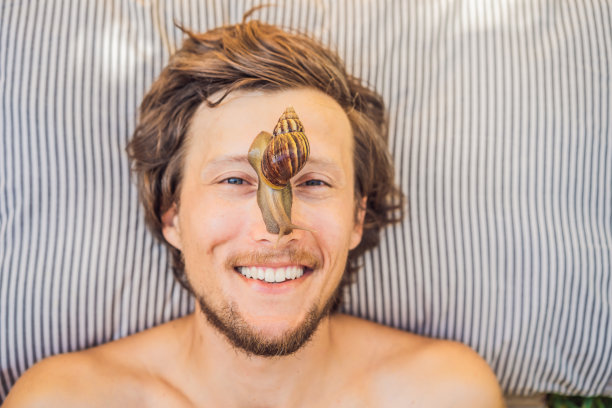 一个年轻人用蜗牛粘液做了一个面膜。蜗牛在口罩上爬行。男士水疗，大众水疗图片下载