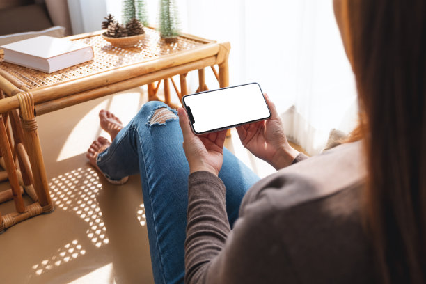 一个女人在家里拿着并使用手机，手机的桌面是白色的图片下载