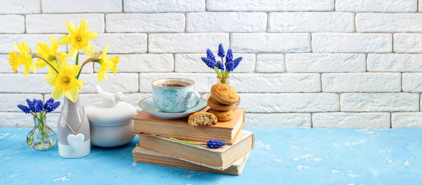 蓝色的桌子上放着一束束春天的鲜花、咖啡杯、书籍和饼干，背景是白色的砖。阅读和早餐。概念春天，hygge和舒适的家庭内部图片下载