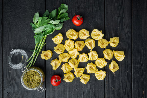 黑色木桌背景上，放着罗勒和松香蒜酱的生意大利饺子，平躺着俯视图图片下载