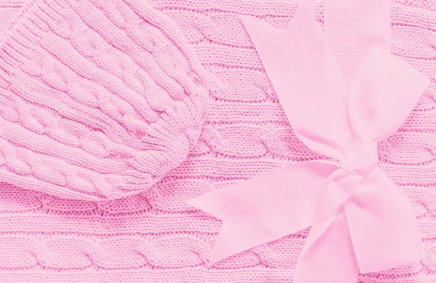 婴儿在柔软的粉红色毯子上编织帽子。可爱的礼物新生儿带蝴蝶结图片下载