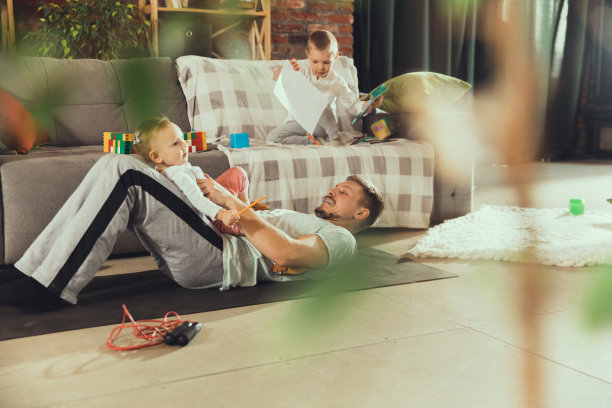 年轻人在家健身，有氧运动，瑜伽，运动生活方式。当他的孩子在后台玩的时候，他变得活跃起来，家里的健身房。图片下载