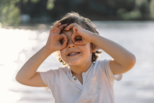 可爱的男孩在河边玩耍和展示大自然中的眼镜图片下载