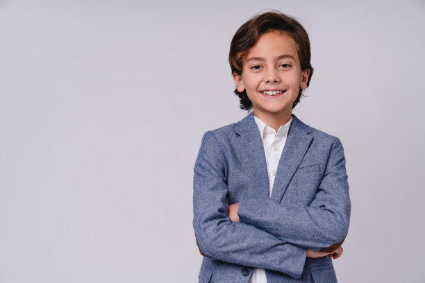 小男孩穿着正式的服装，双臂交叉，孤立在灰色的背景下图片下载