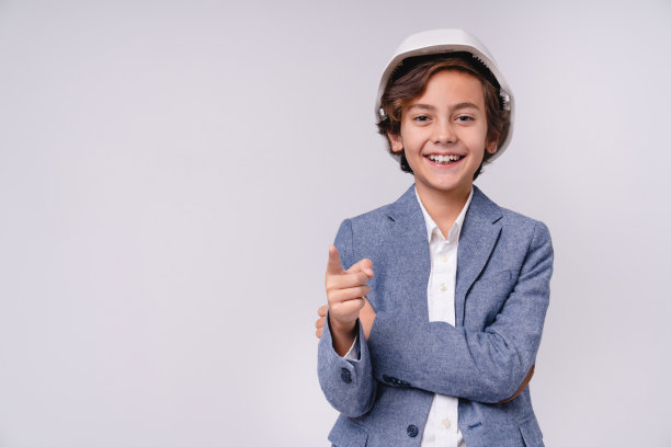 开朗的小男孩在白色安全帽指着你孤立的灰色背景图片下载