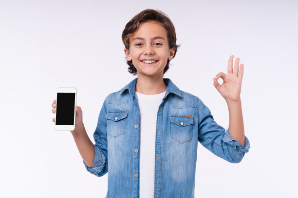 年轻的白人男孩显示ok手势与手机孤立在白色背景图片下载