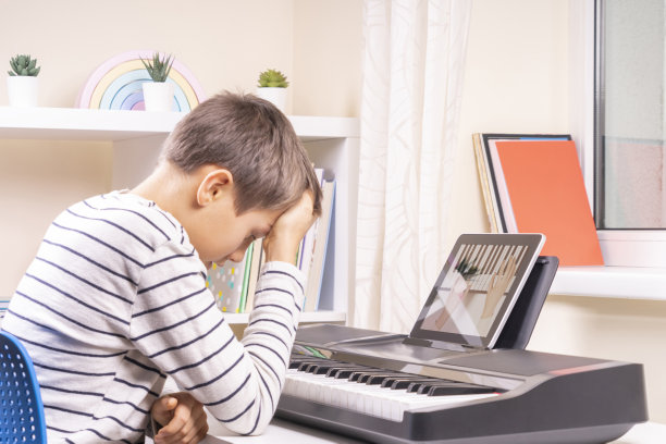 伤心沮丧的男孩在家里很难学弹钢琴。使用数码平板电脑的孩子。在线学习的困难图片下载
