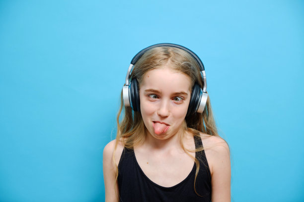戴着耳机的白人小女孩在蓝色背景下闭上了眼睛。情感概念图片下载