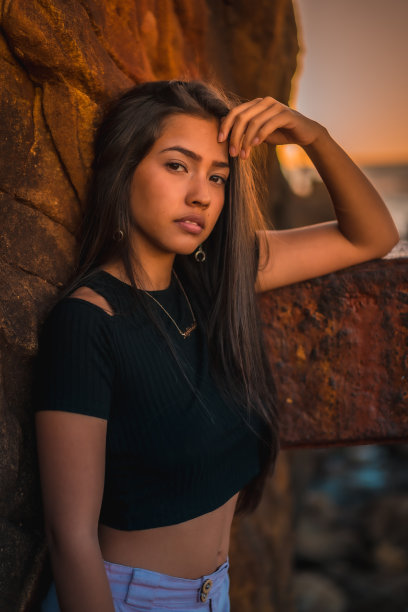 她是一个年轻漂亮的拉丁美人，有着长长的直发，穿着黑色短t恤和粉色裤子。一个女人的肖像倚着一个有痂的雕塑图片下载