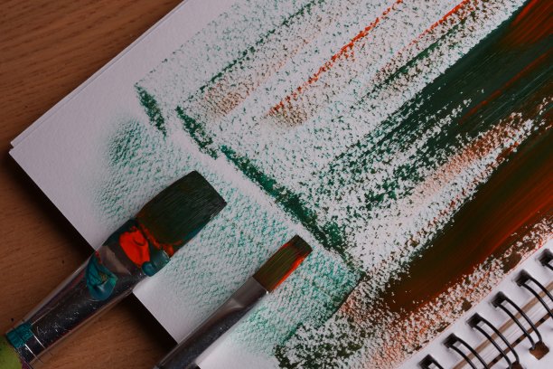 两支毛笔，纸，橙色和绿色的颜料混合在纸上，特写图片下载