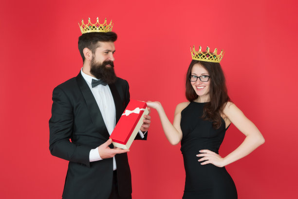 他的心之王后。男子大胡子国王在燕尾服金色皇冠赠送礼盒女子优雅的服装。皇室家族。一对相爱的皇室夫妇。社会精英。国王和王后的正式活动。皇家礼物图片下载