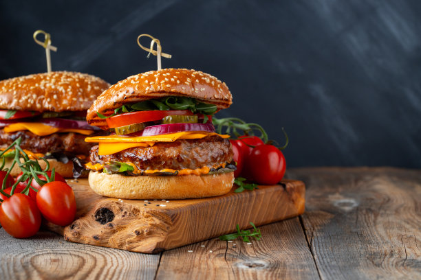 在一张旧木桌上放着两个美味的自制牛肉、奶酪和蔬菜汉堡。脂肪不健康食物特写。与复制空间图片下载