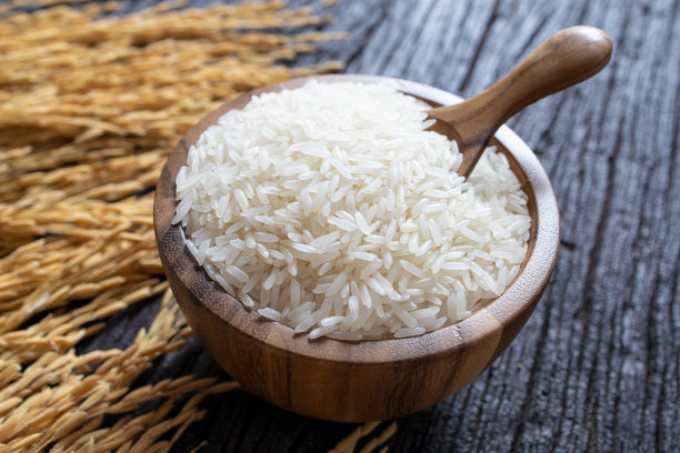 白米(泰国茉莉花米)与木勺木碗和水稻在深色木质纹理的背景。图片下载
