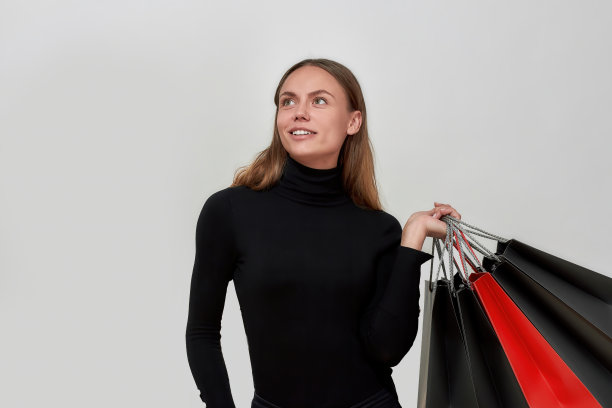 工作室拍摄的漂亮的年轻白种女人穿着黑色衣服看起来很梦幻，拿着一堆购物袋，在浅灰色的背景下摆出孤立的姿势图片下载
