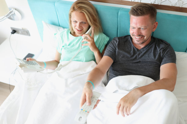 男人和女人躺在床上。女人在打电话，男人打开遥控器按钮图片下载