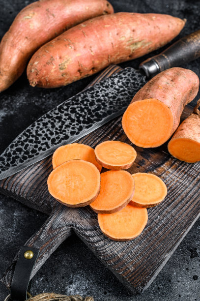 木砧板上的红薯。黑色背景。俯视图图片下载