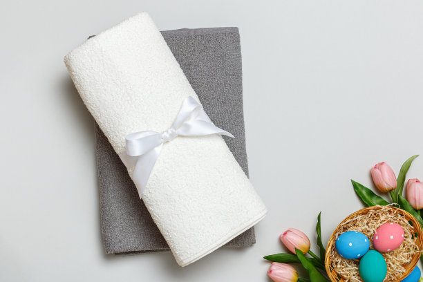 俯视图一堆白色和灰色的毛巾和一个装满彩蛋的复活节篮子。图片下载