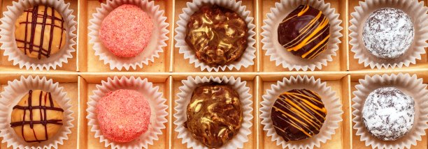 这是一套松露巧克力，由黑巧克力和牛奶巧克力制成，配以橘汁，草莓(蔓越莓，覆盆子)，椰子和糖粉。装在工艺盒里的糖果礼物。横幅,长照片图片下载