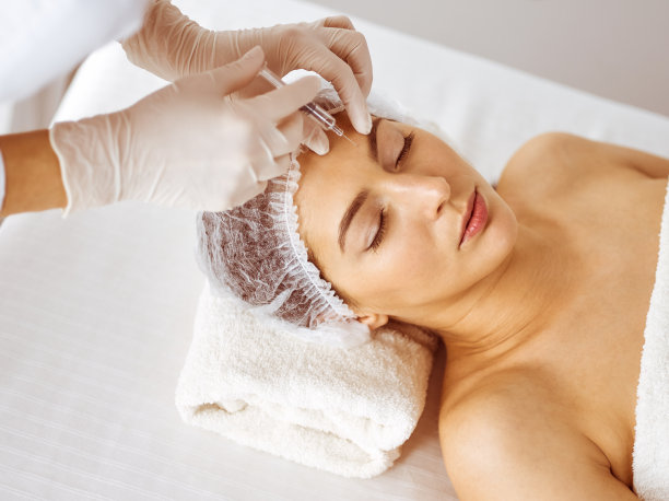 美容师做美容程序与注射器面对年轻的黑发女子。美容药物和手术，美容注射图片下载