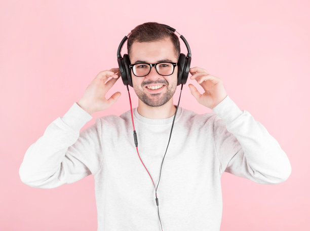快乐的年轻可爱的男孩听音乐在一个大的白色耳机在粉红色的背景，抱着他们，在一个白色的运动衫，带着灿烂的微笑，世界dj日图片下载