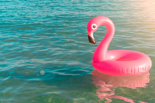 夏天有趣的海滩。粉红色的充气火烈鸟在蓝色的海水在夏季海洋海滩的背景。有趣的小鸟玩具的孩子。图片下载