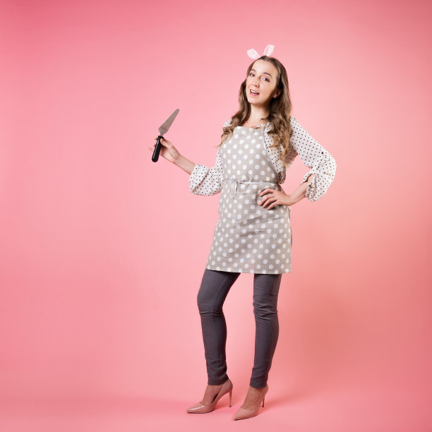 年轻迷人的糕点师手里拿着一把抹刀。一个穿着圆点围裙的厨师。图片下载