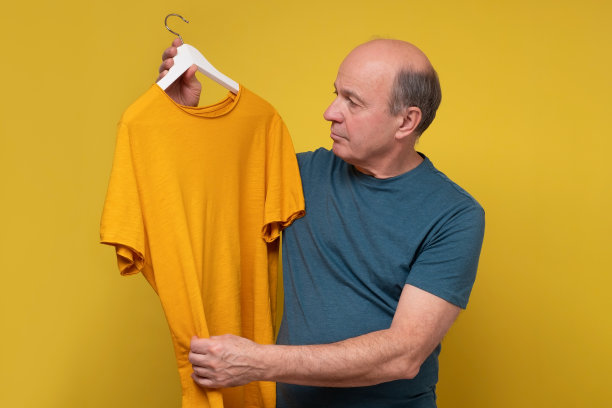 高级男子试图选择一件t恤，而不是黄色背景图片下载