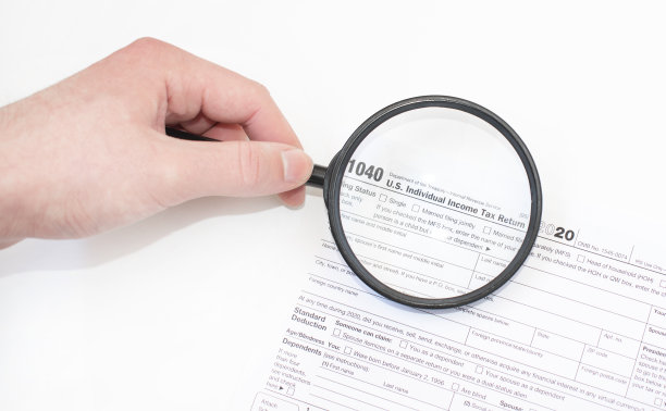 1040年联邦政府个人所得税申报表的特写照片放在一个白色信封里，一个男人拿着放大镜在上面放大它的文字。图片下载