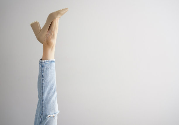 一个穿着牛仔裤和鞋子的年轻女子的腿在一个灰色的背景，文字空间。图片下载