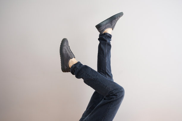 灰色背景下一个穿着牛仔裤和鞋子的年轻人的腿。图片下载