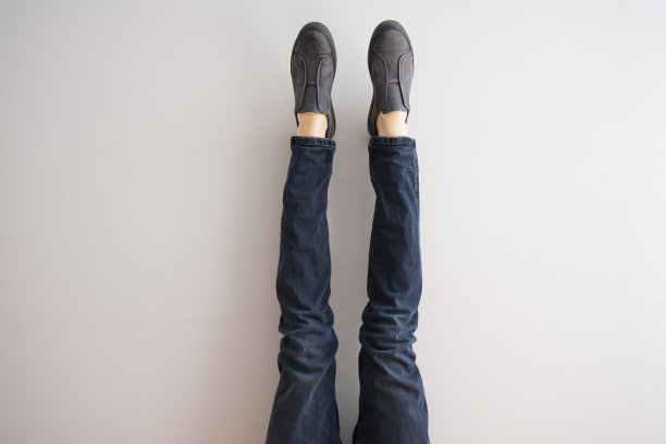 灰色背景下一个穿着牛仔裤和鞋子的年轻人的腿。图片下载
