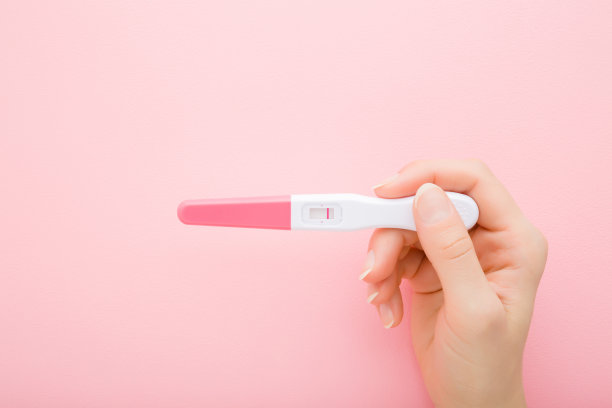 年轻的成年女性手拿妊娠试验与浅粉红色背景上的一条条纹。柔和的颜色。负面的结果。特写镜头。自顶向下的观点。图片下载