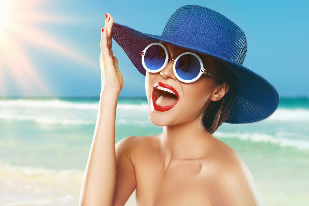 戴着蓝帽子和太阳镜的漂亮女人享受海滩度假图片下载