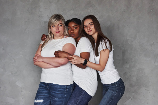 在同样的衣服。在灰色背景下，一群多民族妇女站在演播室里图片下载