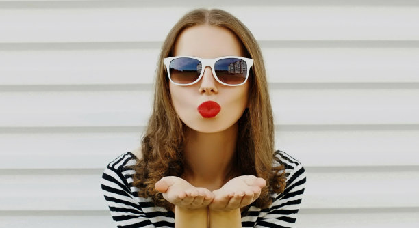 美丽的年轻女子的肖像吹她的红色嘴唇发送甜蜜的空气吻在白色的背景图片下载