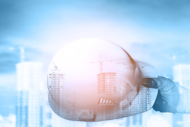 工作场所安全的概念。双重曝光，一名男子的手拿着施工头盔，背景是正在施工的建筑。拼贴画。图片下载