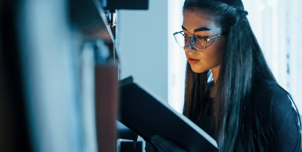 想象的力量。光线从书中出来。女学生在堆满书的图书馆里。教育的概念素材图片