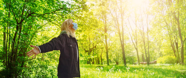 年轻女子戴着医用防护口罩在户外大自然中。图片下载