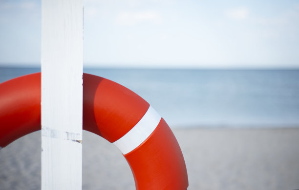 一个橙色的救生圈挂在沙滩上的一根白柱上。海平线和文本复制空间。图片下载