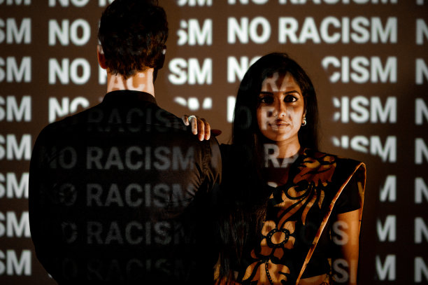 年轻女子穿着传统的服装，严肃地看着镜头旁边的白人男子，黑色背景的放映机灯光照亮图片下载