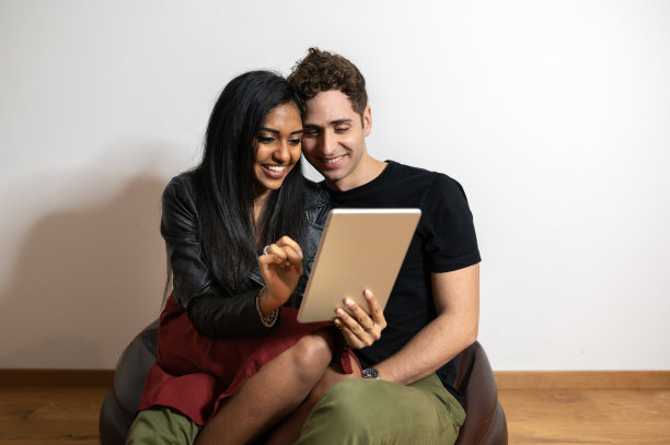 愉快的多民族夫妇在家里的豆袋沙发上浏览平板电脑图片下载