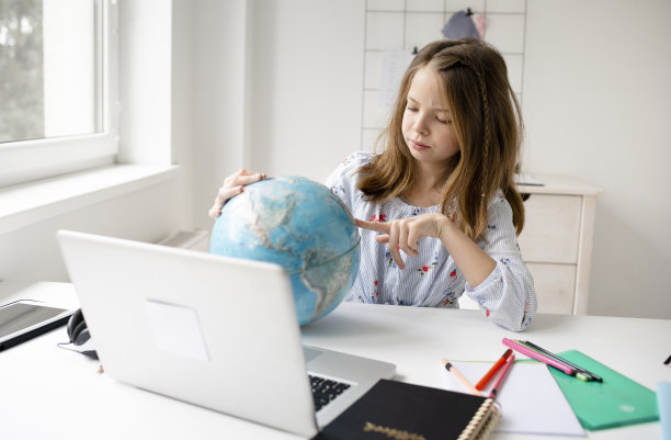 女孩坐在笔记本电脑前，手里拿着地球灯，梦想着假期和瘟疫的结束图片下载